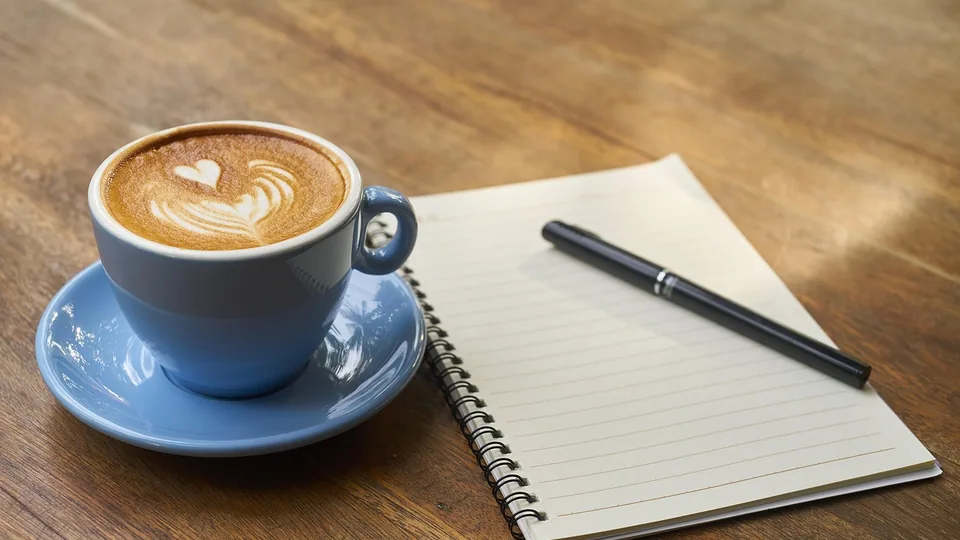 Blankt anteckningsblock med penna bredvid en kaffekopp
